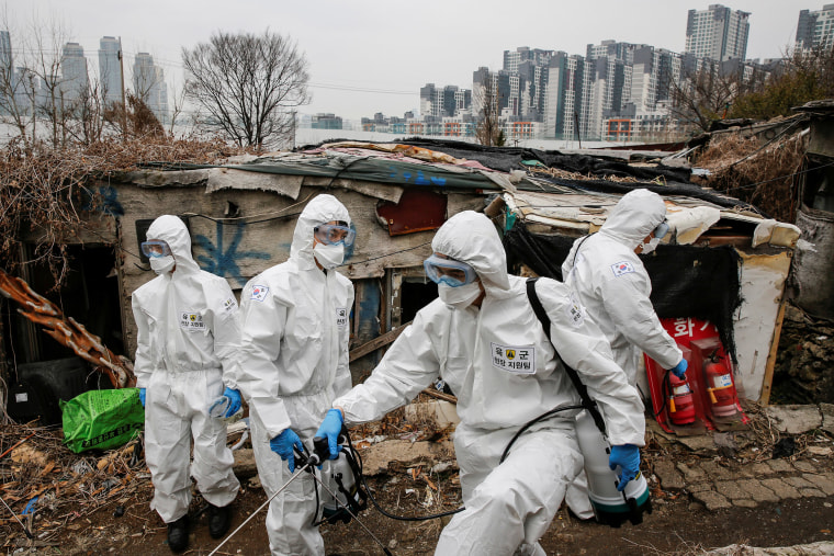 Imagen: Soldados surcoreanos en engranajes protectores desinfectan las chozas mientras se ve un lujoso complejo de apartamentos de gran altura en el fondo en la aldea de Guryong en Seúl