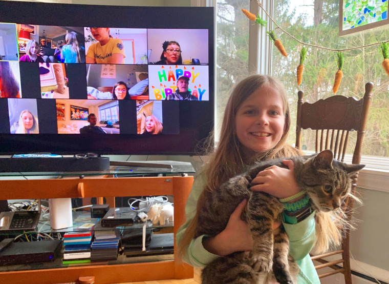 A girl holds a cat during her Zoom birthday party.