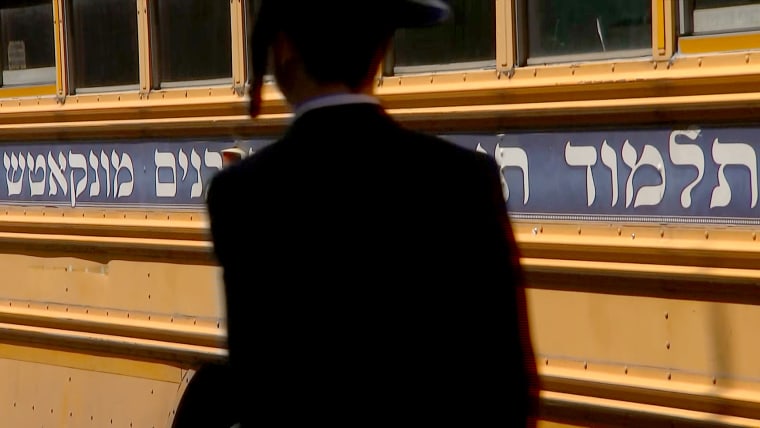 An Orthodox Jewish man walks in front of a school bus in the predominantly Hasidic neighborhood of Borough Park in Brooklyn, N.Y.