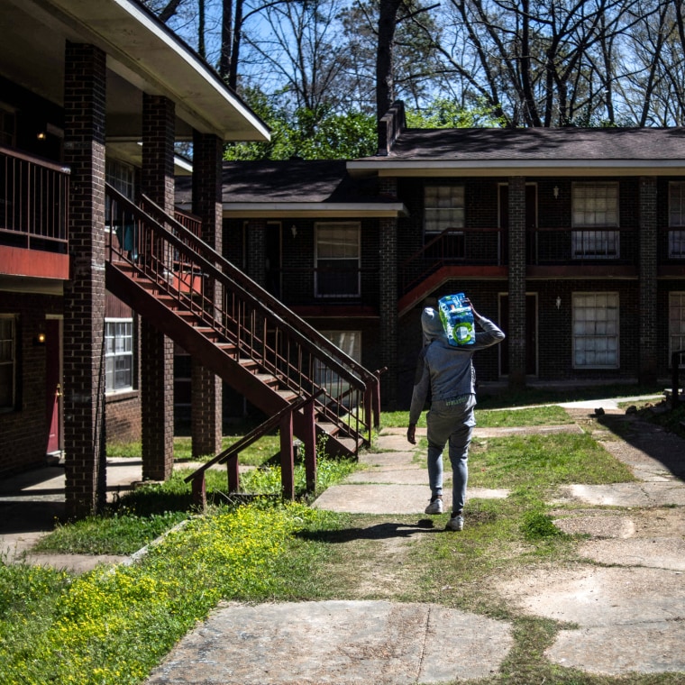 A man carries a case of water through an apartment complex in Jackson, Miss., on March 24, 2022.